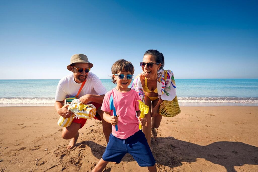 Sommerurlaub 2026 buchen – Familie mit Sonnenbrille am Sandstrand am Mittelmeer