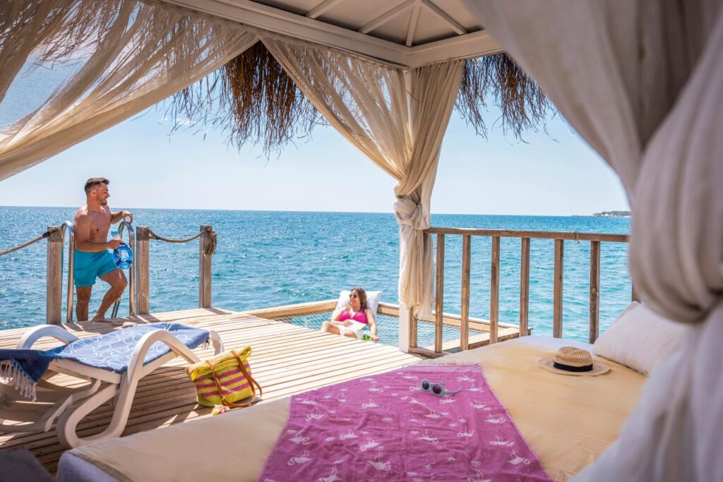 Sommerurlaub 2026 – Paar genießt Meerblick von Pavillon auf Holzsteg am Strand
