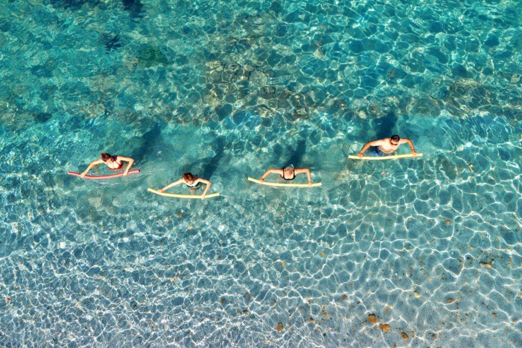 Gruppe macht Aqua-Fitness-Übungen im türkisfarbenen Pool von oben fotografiert