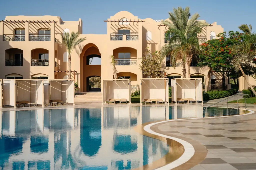 Ruhiger Poolbereich im TUI MAGIC LIFE Redsina mit geschwungenem blauen Pool, weißen Sonnenliegen, beigefarbenen Hotelgebäuden im arabischen Stil und Palmen