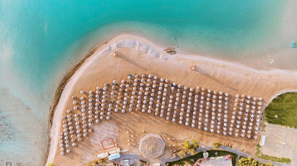 Drohnenaufnahme von oben zeigt den privaten Strandabschnitt des TUI MAGIC LIFE Kalawy mit türkisblauem Wasser, Sandstrand, aufgereihten Sonnenschirmen und grüner Vegetation