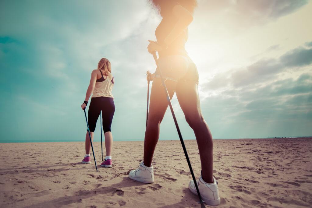 Zwei Frauen mit Nordic-Walking-Stöcken auf sandigem Strand bei Sonnenuntergang beim TUI MAGIC LIFE Events