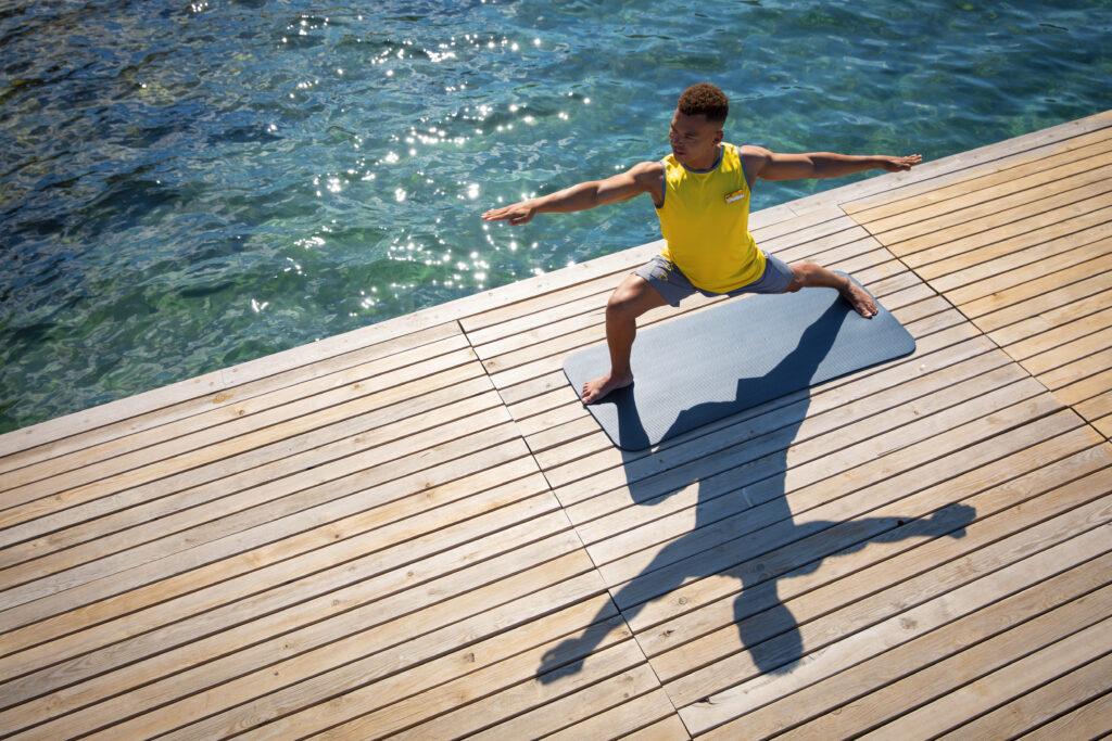 Personen machen Yoga-Übungen auf bunten Matten am Sandstrand im Sonnenuntergang