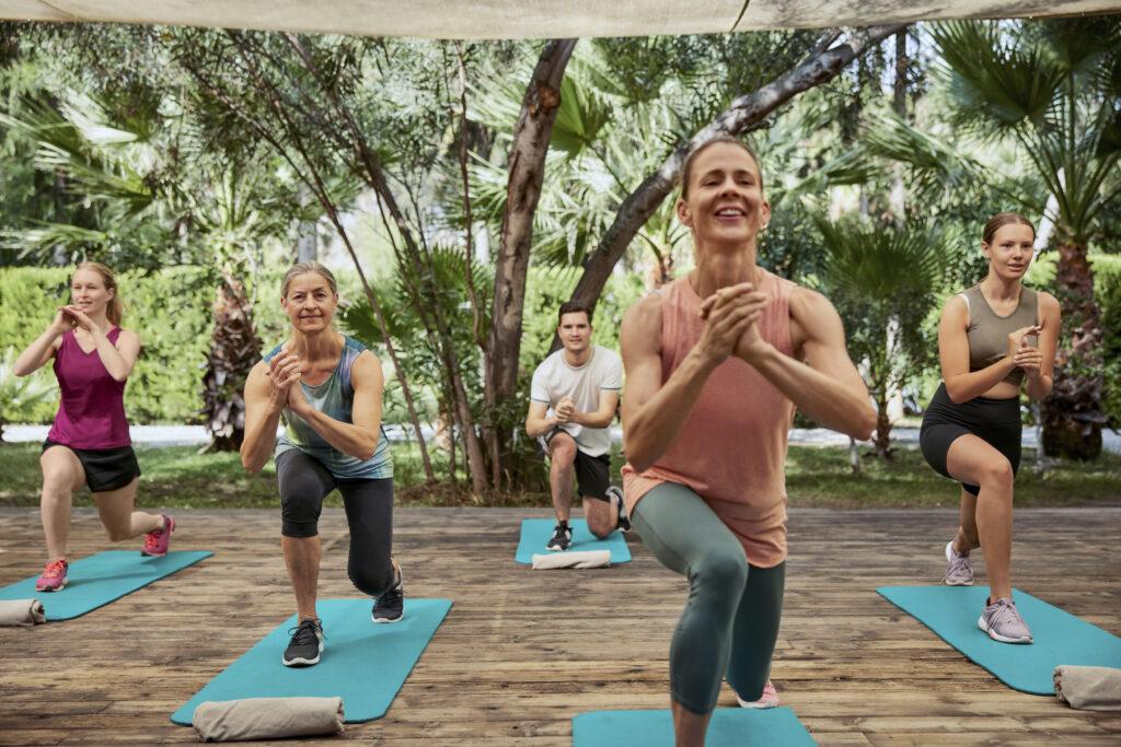 Gruppe von Frauen bei Fitnessübungen auf türkisfarbenen Matten unter Palmen