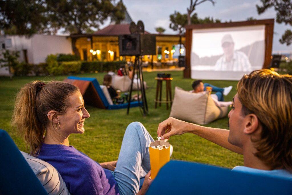 Paare schauen gemeinsam einen Film im Open-Air-Kino des TUI MAGIC LIFE Beldibi, umgeben von entspannter Clubatmosphäre.