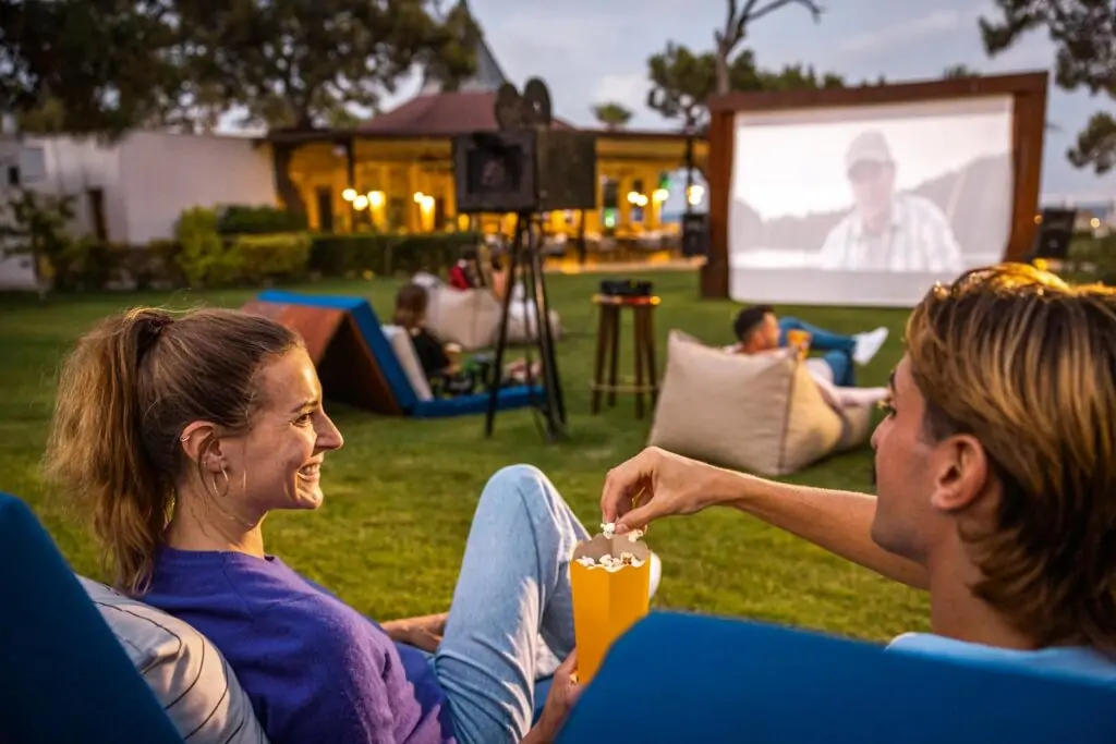 Paare schauen gemeinsam einen Film im Open-Air-Kino des TUI MAGIC LIFE Beldibi, umgeben von entspannter Clubatmosphäre.
