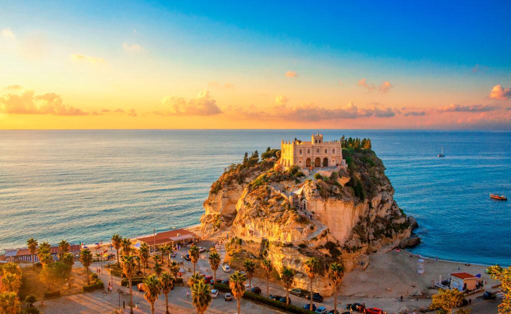 Sonnenuntergang über der Wallfahrtskirche Santa Maria dell'Isola in Tropea, Kalabrien - das Wahrzeichen der Stadt steht auf einem Felsen im Meer vor goldenem Abendhimmel