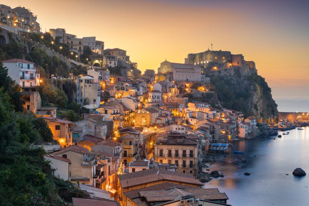 Sonnenuntergang in Scilla an der Meerenge von Messina, Kalabrien - das pittoreske Fischerdorf Chianalea mit bunten Häusern am Wasser und der historischen Burg Ruffo auf dem Felsen, bekannt als "Venedig des Südens"