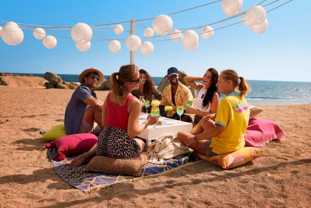 Gruppe beim Strand-Picknick im Singles Urlaub All Inclusive Resort mit bunten Lampions und Meerblick