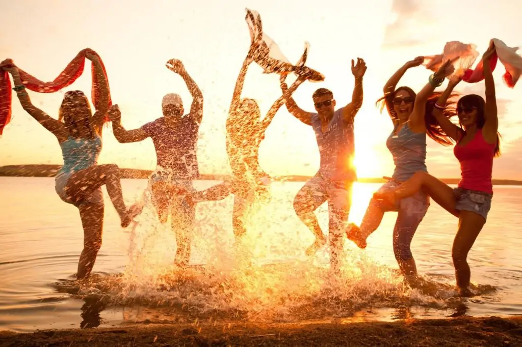 Singles Urlaub All Inclusive: Fröhliche Strandmomente im warmen Abendlicht, gemeinsamer Spaß im Wasser vor traumhafter Kulisse.