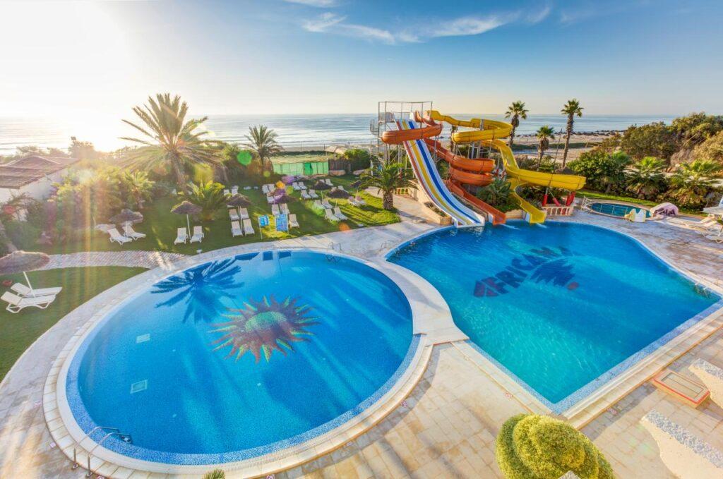 Panoramaansicht Hotelaquapark mit geschwungenen Wasserrutschen, zwei türkisblauen Pools und Meerblick Hammamet