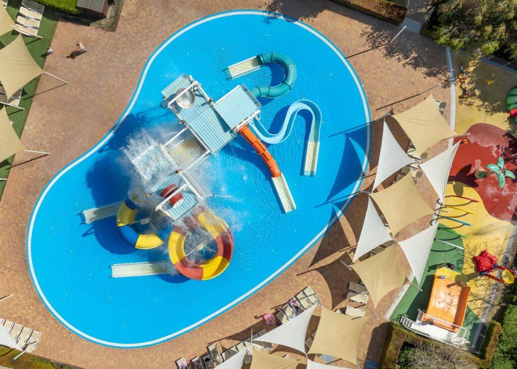 Luftaufnahme des Splashparks im TUI MAGIC LIFE Calabria in Italien mit bunten Wasserrutschen, Wasserfontänen und Poolbereich für Kinder und Erwachsene.