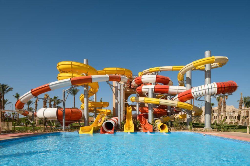 Blick auf den Aquapark im TUI MAGIC LIFE Redsina Sharm El Sheikh mit mehreren gelben, weißen und roten Wasserrutschen, die in einen großen Außenpool münden.