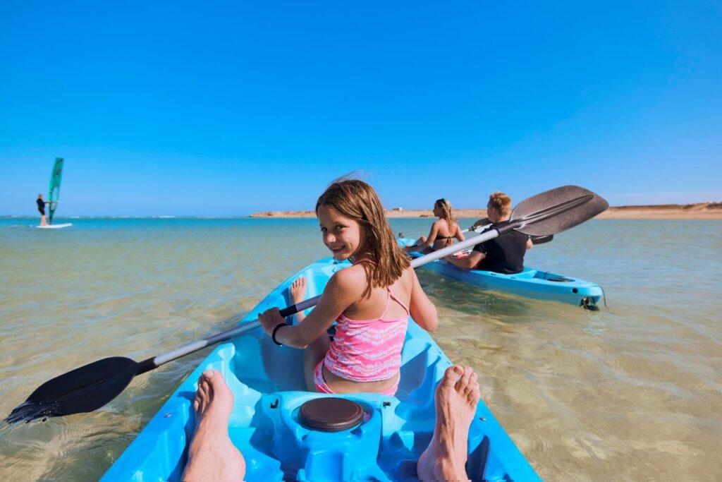 Familie paddelt im Kajak auf klarem, blauem Wasser und genießt eine aktive Wassersportaktivität während des Urlaubs.