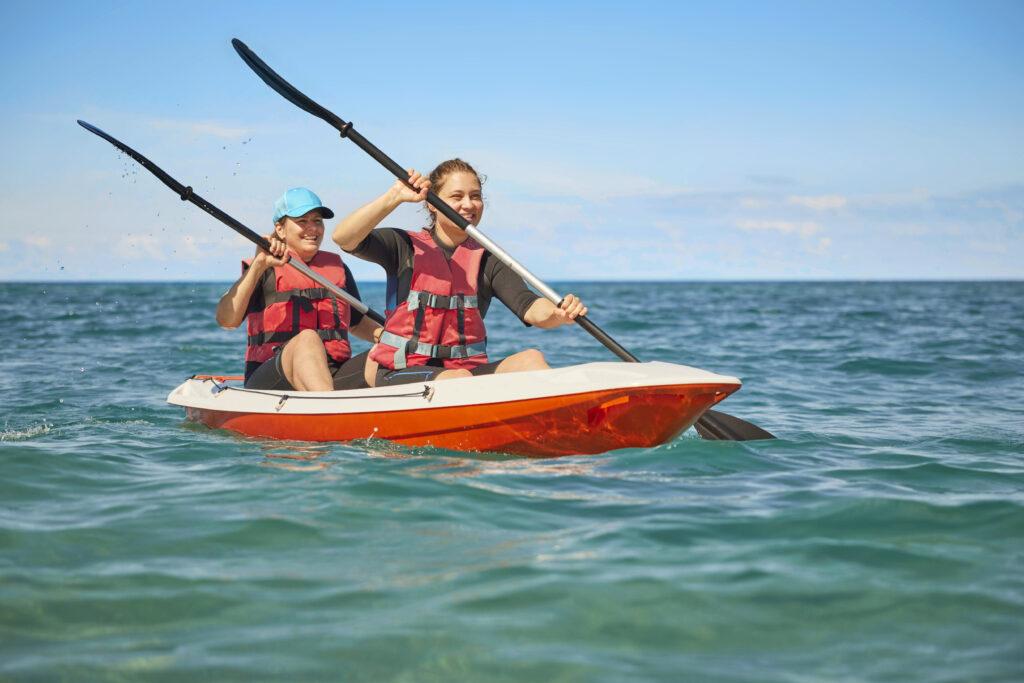 Kajak-Tour auf türkisblauem Meer Kalabrien - Erwachsener und Kind paddeln gemeinsam im roten Kajak mit Schwimmwesten, beliebte Aktivität im Familienurlaub
