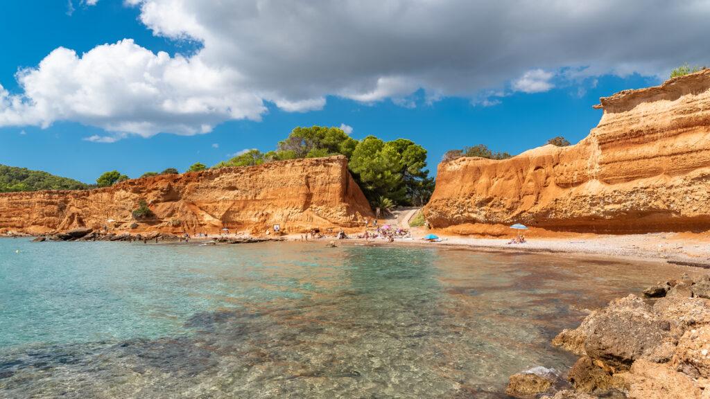 Blick auf den Strand Sa Caleta auf Ibiza mit roten Felsen, klarem Meer und kleiner Badebucht.