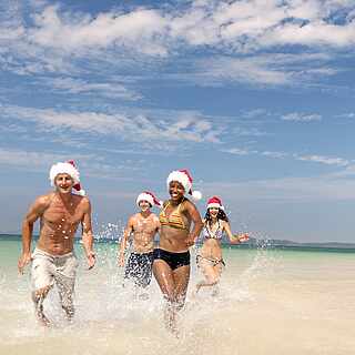 Freunde laufen mit Weihnachtsmütze am Strand 
