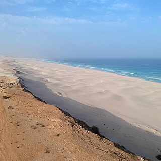 Wüstenartiger Strandabschnitt der auf feinen Sand und blaues Wasser trifft unter blauem Himmel