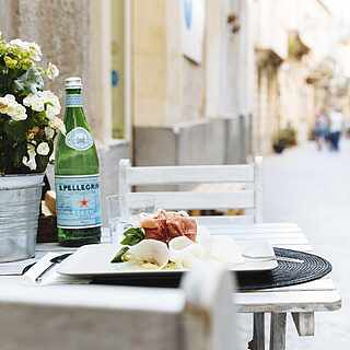 Gedeckter Tisch mit Wasser und Schinken in einer hübschen Gasse in Italien
