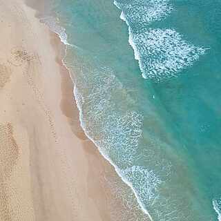 Blick von Oben auf türkises Meer und feinen Sandstrand