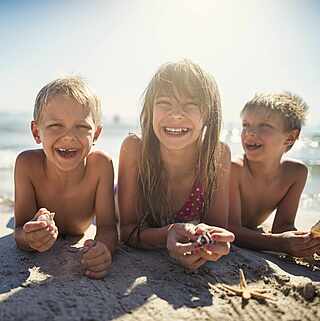Ein Mädchen und Zwillingsbrüder, die bäuchlings am Strand liegen. 